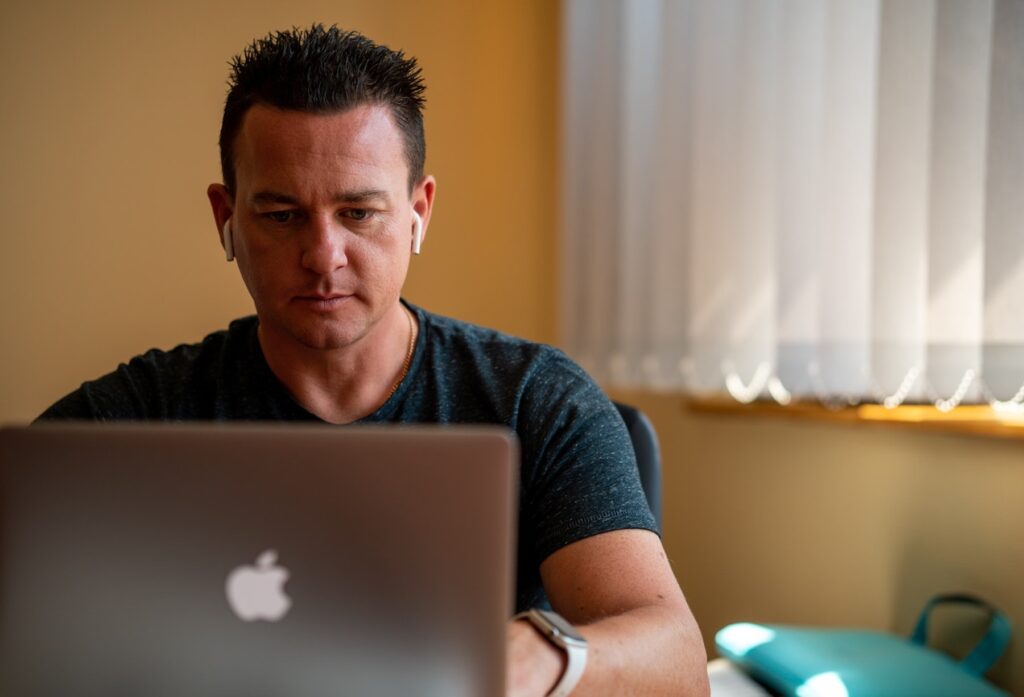 An online learner works on his laptop in his bedroom wearing airpods