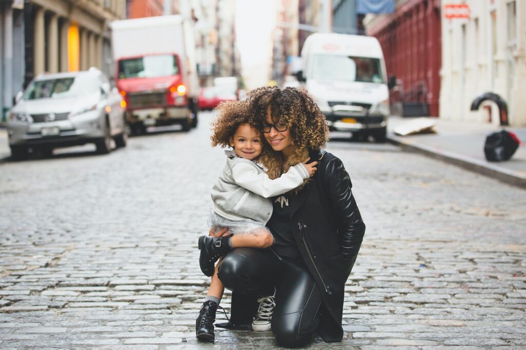 A mom hugs her daughter with a city street and cars in the background