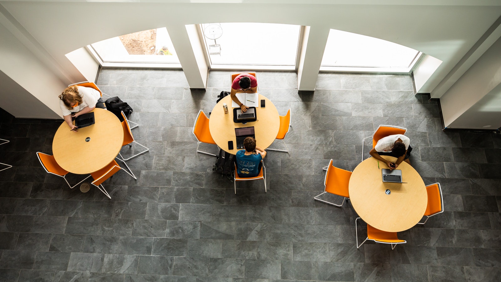 An interior aerial view of UTK BAIP students studying at round tables with orange chairs