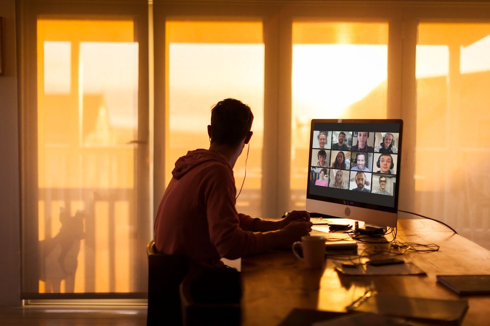 A person looks out a window as they sit in front of a computer while on a video call.