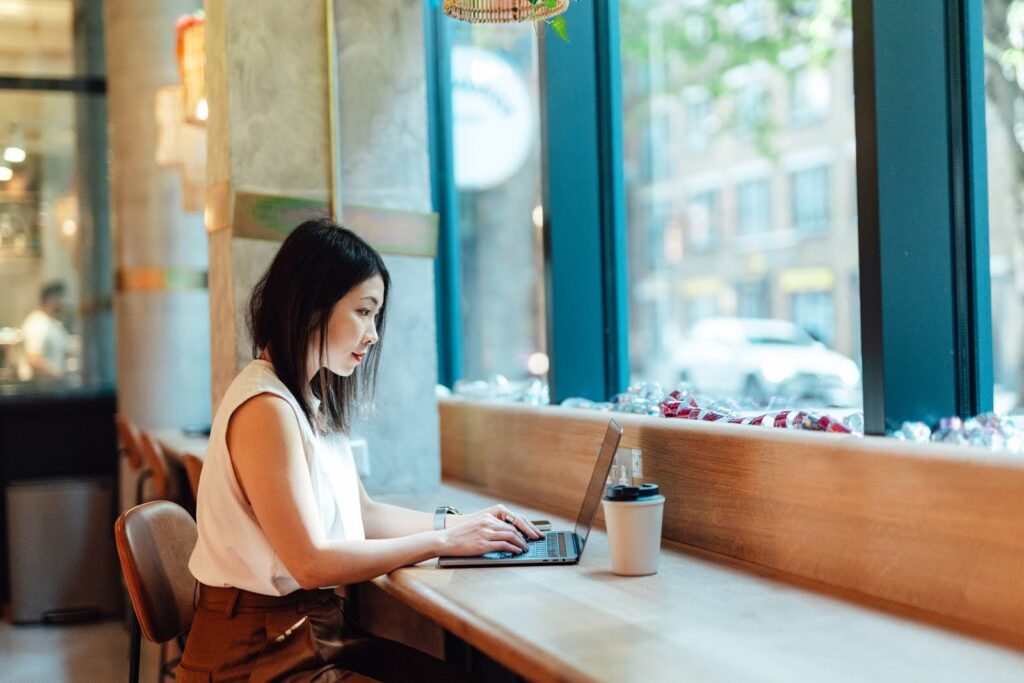 A woman in a coffee shop types on a laptop computer.