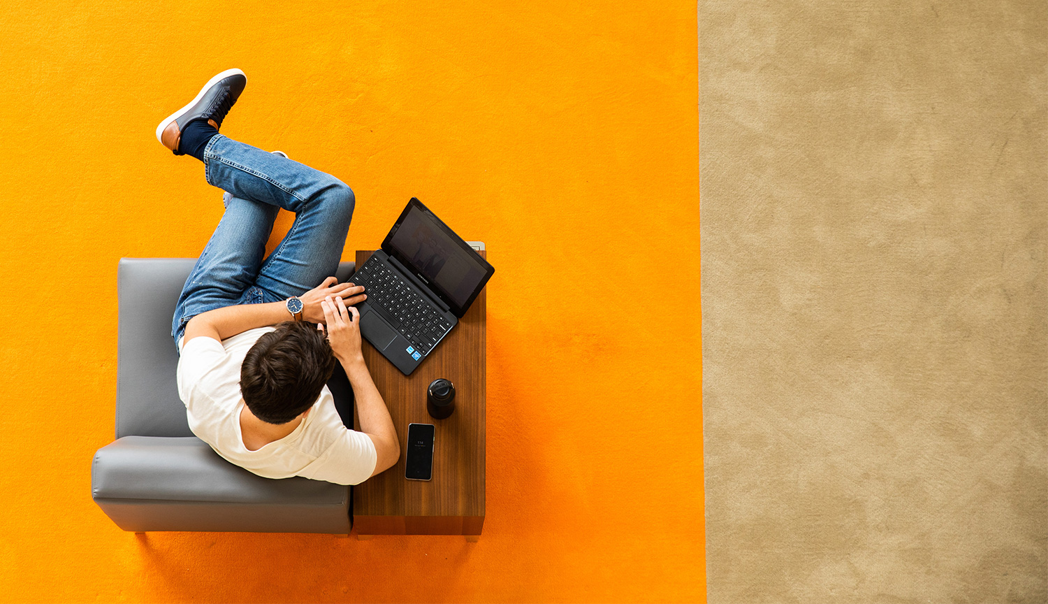 An aerial view of a seated student working on a laptop, situated on top of an orange rug.